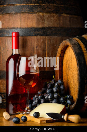 Rose wine bootle and glass, cheese and grapes in still life on wooden barrel background Stock Photo