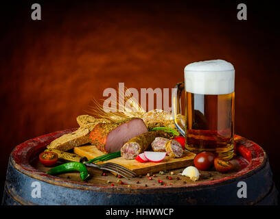 One mug of beer on a wooden barrel, and smoked sausages  and vegetables in still-life Stock Photo