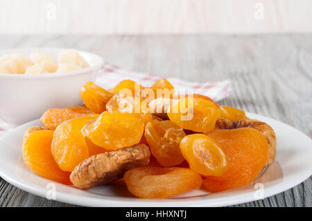 Dried fruits in white plate on a wooden background. Candied pineapple, lemon, apricot, figs. Stock Photo