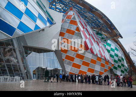 Queue of visitors to the Fondation Louis Vuitton in the Bois de Boulogne in Paris, France. People wait for the security control to visit the exhibition Icons of Modern Art from the Shchukin Collection. The exhibition runs till 5 March 2017. The building designed by architect Frank Gehry was completed in 2014. Coloured filters on the glass sails are the temporary installation in situ entitled Observatory of Light (2016) by French artist Daniel Buren. Stock Photo