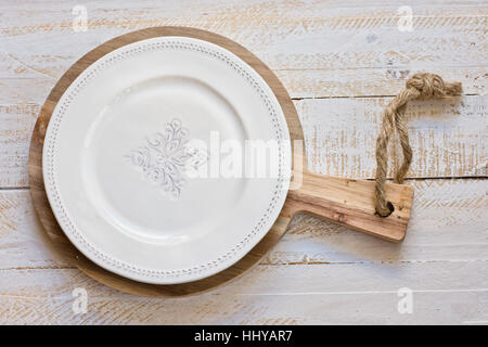 White vintage empty plate on round cutting board, white plank wood background, Provence style, kitchen interior, minimalistic Stock Photo