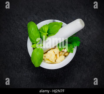 Top View of Pestle and Mortart with Green Basil Herbs, Parmesan Cheese and Pine Nuts on Dark Background Stock Photo