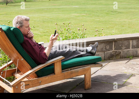 Mature Man with PDA Relaxing on Chaise Lounge Chair on Flagstone Deck in Back Yard Stock Photo