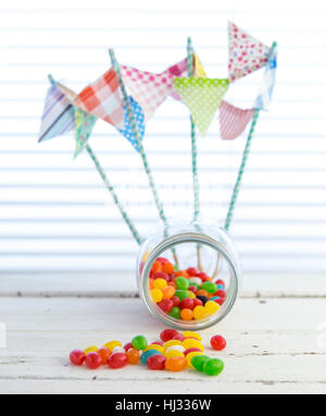 Colorful jellybeans spilling from a Jar with white rustic background Stock Photo