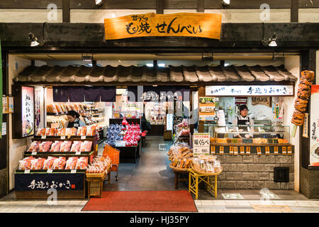 Japan, Matsuyama. Dogo shopping mall. Night time, interior. Looking into open-fronted shop selling rice crackers and sweets, with take-away counter. Stock Photo