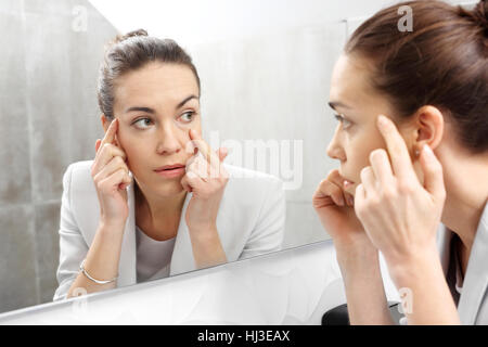 Reflection in the mirror. Woman looks in the mirror noticing the first wrinkles Stock Photo