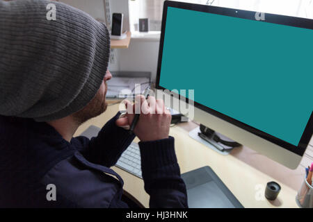 Creative man sat at desk working on designs on a computer using a graphics tablet Stock Photo