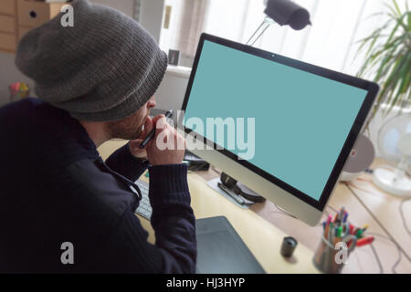 Creative man sat at desk working on designs on a computer using a graphics tablet. Stock Photo