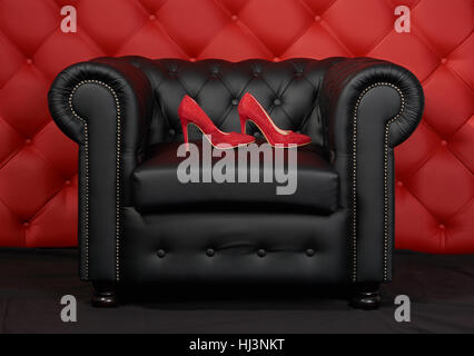 Pair of red women's shoes with rhinestone on black leather armchair. Red leather carriage upholstery on the background. Stock Photo