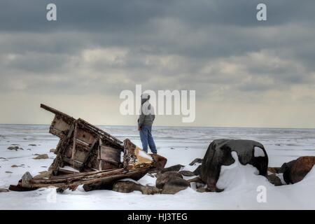 Shipwreck Island. Teenager in a hoodie standing by a shipwreck looking over a desolate winter landscape.