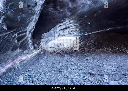 A volcanic ice cave in Iceland takes on the color of the black volcanic dirt surrounding the glacier from which the cavern was formed Stock Photo