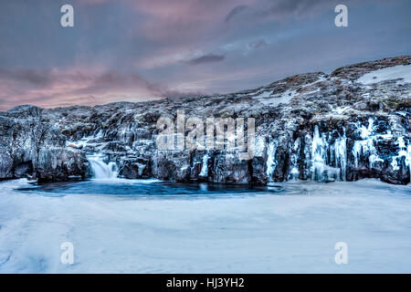 A frozen river in the highlands of Iceland framed by dark pastel skies and rugged terrain offers scenic landscape epitomizing the frozen wilderness. Stock Photo