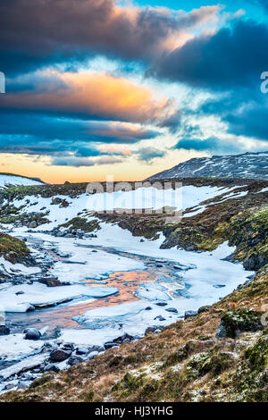 A frozen river in the highlands of Iceland framed by pastel skies and rugged terrain offers scenic landscape epitomizing the frozen wilderness. Stock Photo