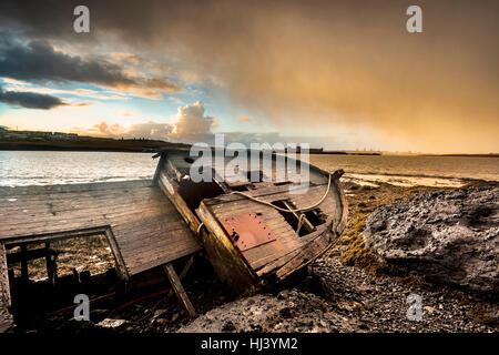 An old abandoned fishing vessel from the early 1900's rests on a remote beach as it rots, exposing the ship's wooden ribs and hull infrastructure.
