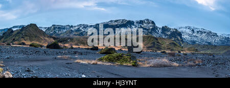 An Iceland mountain range panorama shows the snow-covered mountaintops with dry volcanic landscape and arctic vegetation surrounding the terrain. Stock Photo