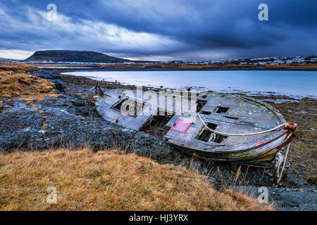 An old abandoned fishing vessel from the early 1900's rests on a remote beach as it rots, exposing the ship's wooden ribs and hull infrastructure. Stock Photo