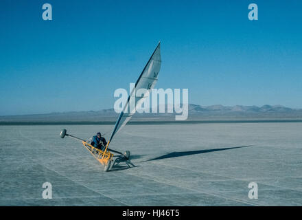 Land sailing in the United States became a popular recreational sport in the 1970s, especially at the flat and vast El Mirage Dry Lake in the Mojave Desert in San Bernardino County, California. The land yachts or sand yachts, as they are called, are three-wheeled vehicles that frequently ride on two wheels when the desert winds are strong. Pilots of these crafts often angle their direction and the sail for an exciting result called 'lifting a wheel,' as shown here. Stock Photo