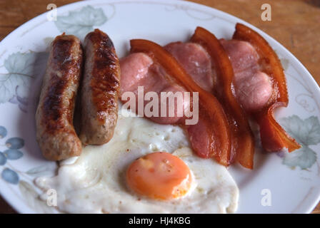 Organic cooked egg, bacon and sausages on a white plate, a popular 'fried' breakfast Stock Photo