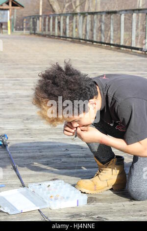 A boy prepares his fishing line on the Rivergreenway footbridge over Spy Run Creek near Lawton Park in Fort Wayne, Indiana, USA. Stock Photo