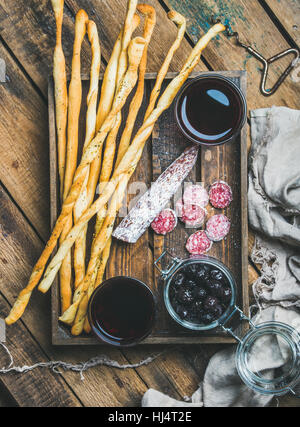 Grissini bread sticks, sausage, black olives, wine in wooden tray Stock Photo