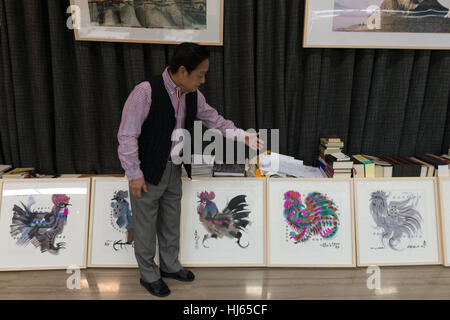 (170126) -- BEIJING, Jan. 26, 2017 (Xinhua) -- Chinese artist Han Meilin, 80, shows his paintings of roosters and hens at his studio in eastern district of Tongzhou in Beijing, capital of China, Jan. 24, 2017. Han, designer of the 2008 Beijing Olympic Games mascot 'Fuwa,' has just finished the design of Chinese zodiac stamps for the upcoming Year of the Rooster. The set of Chinese Lunar New Year rooster stamps, issued earlier this month, contain two items showing a rooster striding proudly and a hen looking after her two chicks. Han applied rich color and elements of traditional Chinese painti Stock Photo