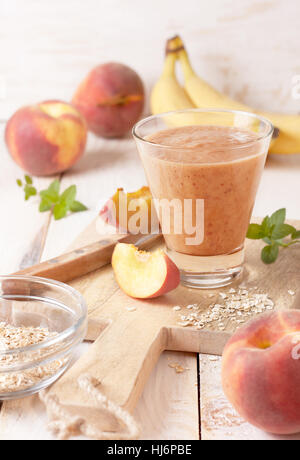 peach banana smoothie with oatmeal  in a glass,  fresh peaches on a wooden background Stock Photo