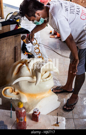 Indonesian guy spray painting an enormous Ogoh-Ogoh demon-like head in Bali for the religious festival parade of Ngrupuk on Balinese New Years Eve Stock Photo