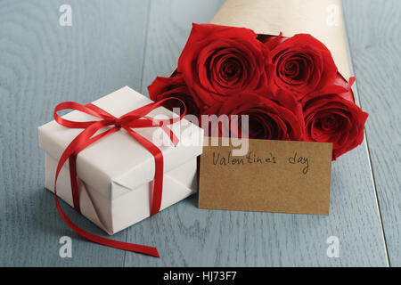 bouquet of red roses on blue wood table with gift and valentines day paper card Stock Photo