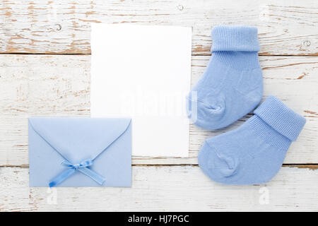 Small boy blue socks, blank card and evelop on white wooden background. Flat lay. Stock Photo