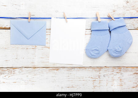 Small boy blue socks, blank card and evelop on white wooden background. Flat lay. Stock Photo