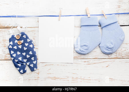 Small boy blue socks, blank card and overalls on white wooden background. Flat lay. Stock Photo