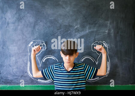 Concepts on blackboard at school. Intelligent and successful latino boy in class standing against blackboard with drawing representing concept of bull Stock Photo