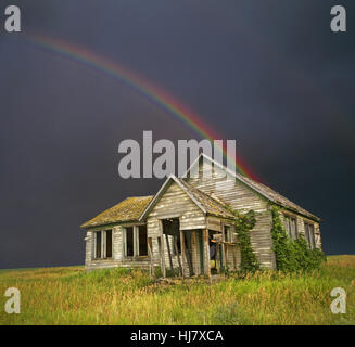 A long abandoned, depression era farm house on the Wyoming plains underneath a stormy summer sky and rainbow Stock Photo