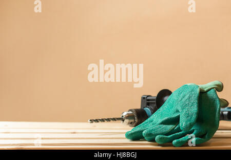 Green working gloves with hammer drill on lining wooden table and copy space wall. Protection workers concept. Stock Photo