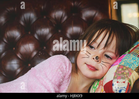 Young girl with Halloween face paint lying on couch Stock Photo