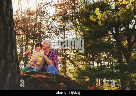 Grandmother and granddaughter sitting in forest hugging Stock Photo