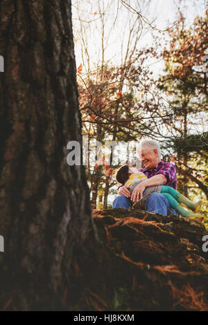 Grandmother and granddaughter sitting in forest hugging Stock Photo