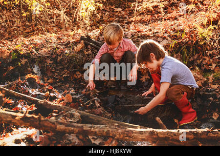 two boys playing in mud by a river Stock Photo