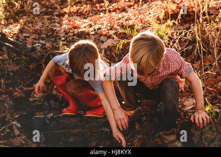 two boys playing in mud by a river Stock Photo