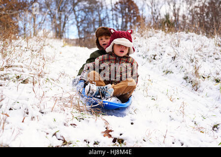 Two children sledding down hill in the snow Stock Photo