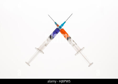 Two syringes holding purple and orange liquid crossing on white background Stock Photo