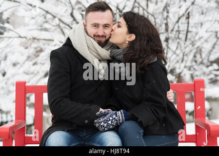 Couple sitting on bench, woman kissing man's cheek Stock Photo