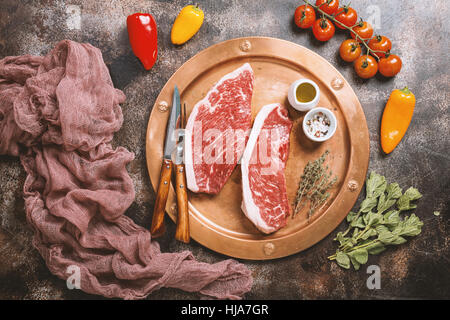 Fresh raw Prime Black Angus beef strip steaks on metal plate over dark rustic concrete background, top view. Ingredients set for making healthy dinner Stock Photo