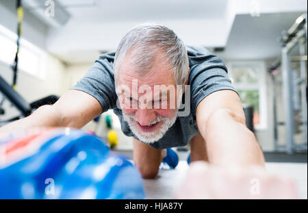 Senior man in gym exercising abs with wheel roller Stock Photo