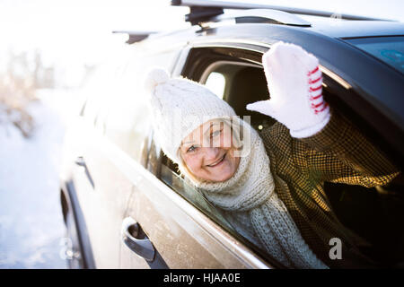 Senior woman in winter clothes in a car, waving Stock Photo