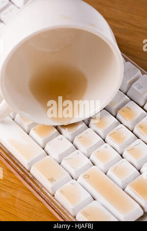 Cup of tea spilled over a keyboard close up on a wooden desk Stock Photo