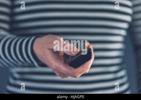 Female hand with television remote control pointing to tv set and turning it on or off Stock Photo