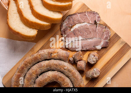 Roasted traditional homemade sausage with spices and herbs and slices spicy meat baked with herbs and spice on wooden cutting board. Stock Photo