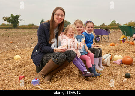 Portrait of mid adult woman and three girls picnicking in pumpkin field Stock Photo