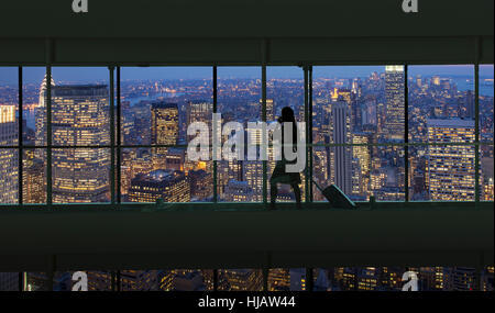 Silhouetted woman crossing city footbridge over New York cityscape at night, USA Stock Photo